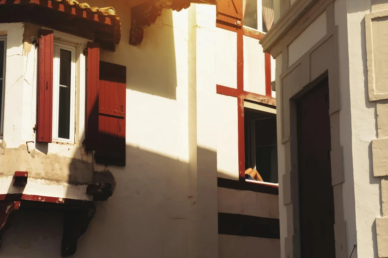 a cat is sitting in the window sill of a building, a photo, inspired by Pieter de Hooch, pexels contest winner, renaissance, sun flare, white buildings with red roofs, 30-year-old french woman, slide show