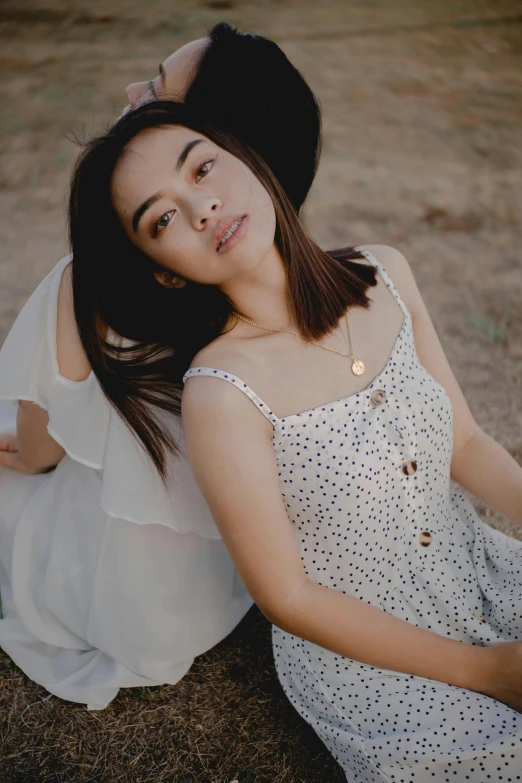 a woman in a white dress sitting on a rock, inspired by Ruth Jên, trending on pexels, renaissance, polka dot, wearing a camisole, arm around her neck, young asian woman