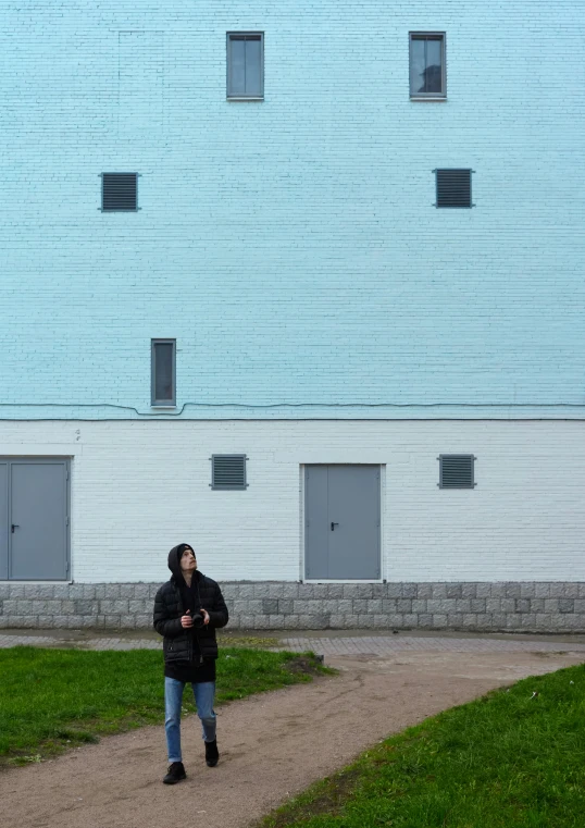 a person walking on a path in front of a building, inspired by Rachel Whiteread, temporary art, blue and cyan colors, tarmo juhola, taking a picture, warehouses