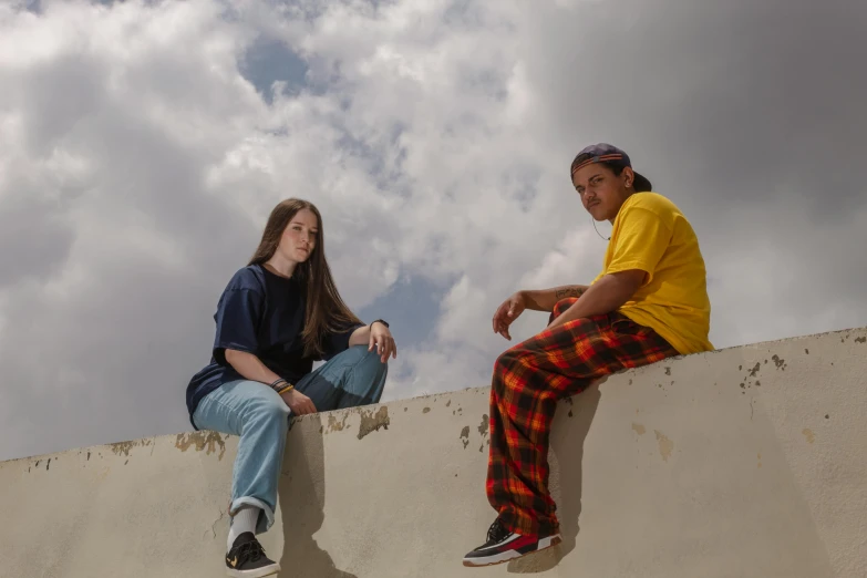 a couple of people sitting on top of a cement wall, a portrait, trending on pexels, realism, in blue and yellow clothes, uniform off - white sky, teenage girl, charli bowater and artgeem