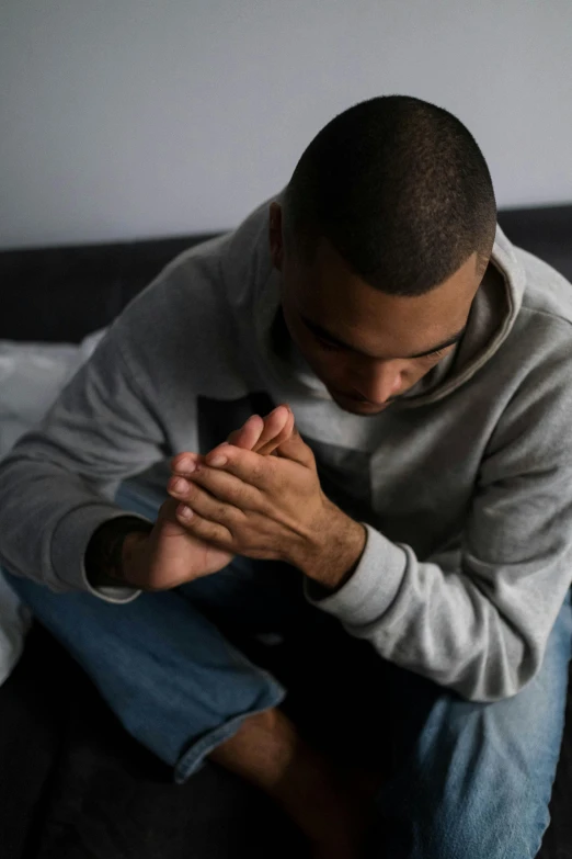 a man sitting on a bed holding his hands together, trending on pexels, renaissance, kneeling in prayer, african american, foot, spasms