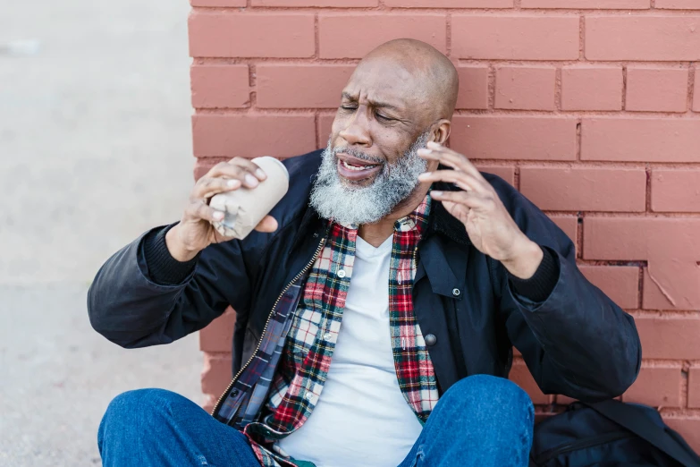 a man sitting on the ground talking on a cell phone, a photo, by Washington Allston, pexels contest winner, hyperrealism, eating garlic bread, bald head and white beard, drinking cough syrup, man is with black skin