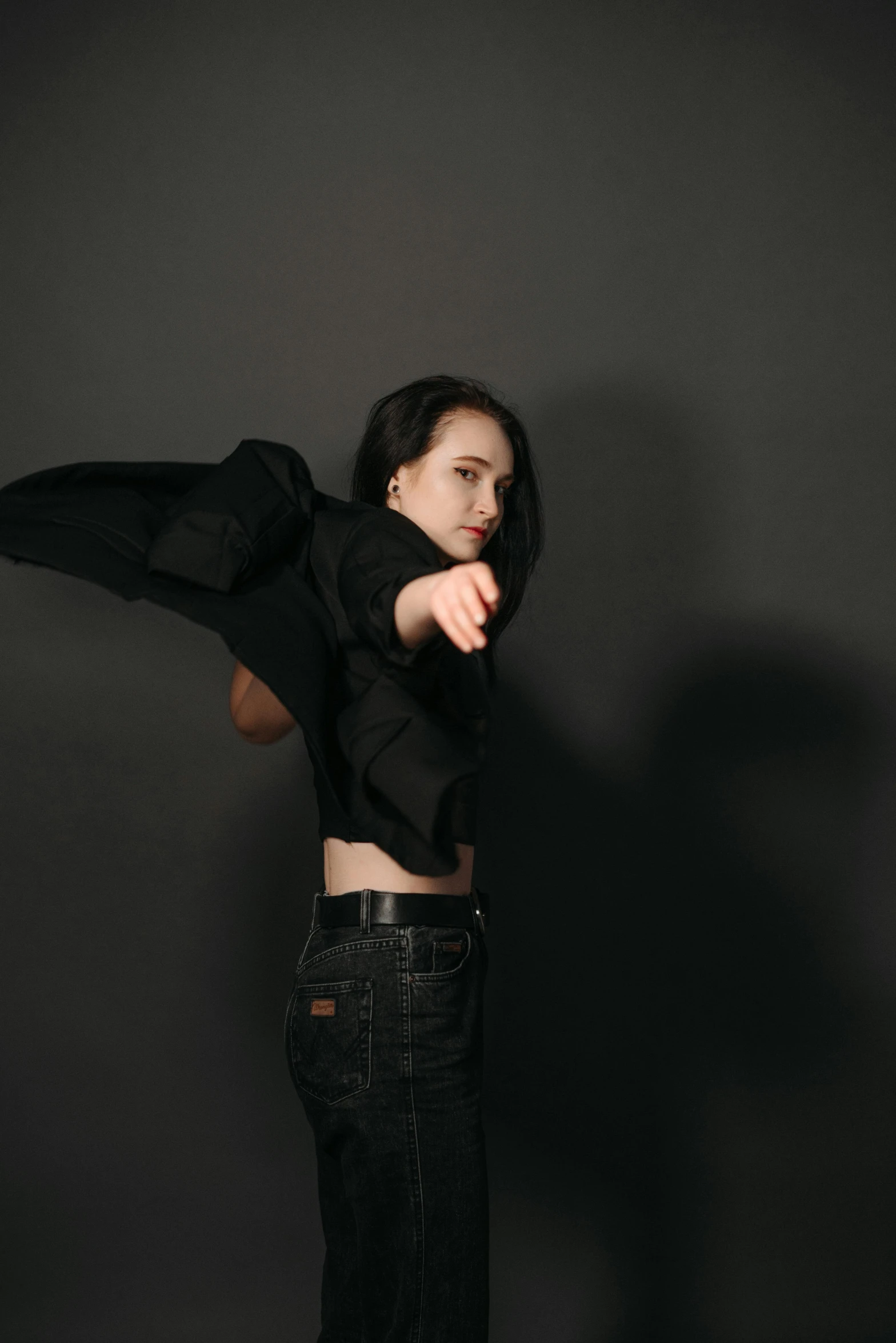 a woman standing in front of a black background, an album cover, unsplash, arms akimbo pose, wearing a black jacket, dilraba dilmurat, fighting pose