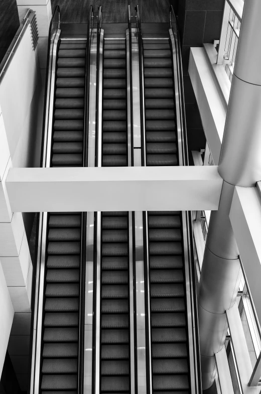 a black and white photo of an escalator, inspired by Andreas Gursky, skybridges, [ overhead view ]!, square lines, two stories