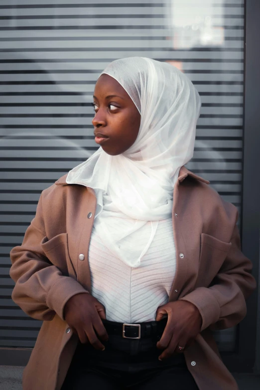 a woman wearing a hijab standing in front of a building, trending on unsplash, with brown skin, white jacket, tight wrinkled cloath, black teenage girl