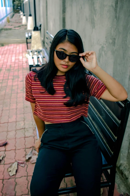 a woman sitting on top of a wooden bench, inspired by Natasha Tan, pexels contest winner, sumatraism, red t-shirt, stripe over eye, street outfit, wearing shades