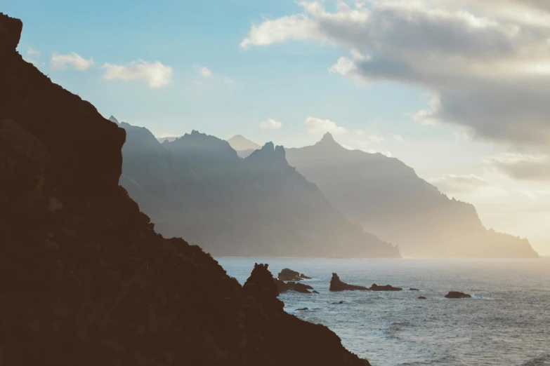 a person standing on top of a cliff next to the ocean, pexels contest winner, romanticism, craggy mountains, late afternoon light, brown, minimalistic background