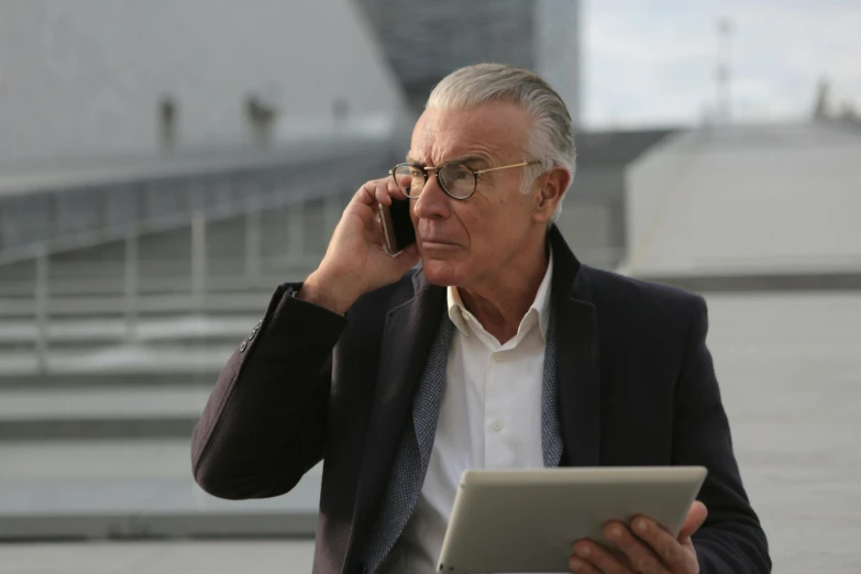 a man sitting at a table talking on a cell phone, dark grey haired man, using a magical tablet, calatrava, avatar image