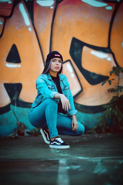 a woman sitting on a skateboard in front of a graffiti wall, a picture, inspired by Rudy Siswanto, trending on pexels, wearing teal beanie, wearing a jeans jackets, avatar image, scary pose