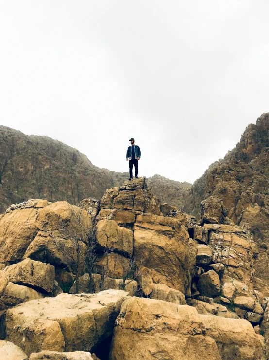 a man standing on top of a pile of rocks, profile image, hicham habchi, overcast weather, in between a gorge