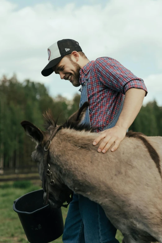 a man standing next to a donkey holding a bucket, by Jaakko Mattila, horse laying down, happy friend, wearing polo shirt, profile image