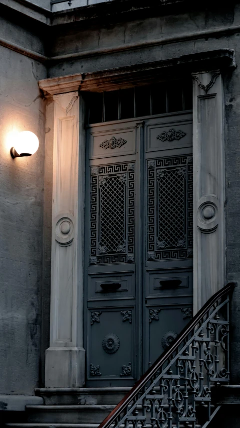 a light that is on the side of a building, by Carlo Martini, pexels contest winner, art nouveau, tall door, charcoal and silver color scheme, evening atmosphere, at home