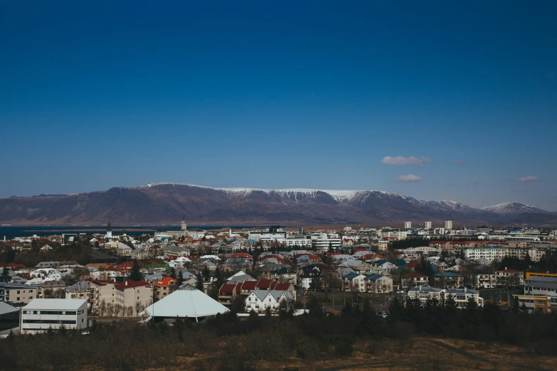 a view of a city with mountains in the background, inspired by Júlíana Sveinsdóttir, pexels contest winner, hurufiyya, reykjavik junior college, clear blue skies, shot on hasselblad, city buildings on top of trees