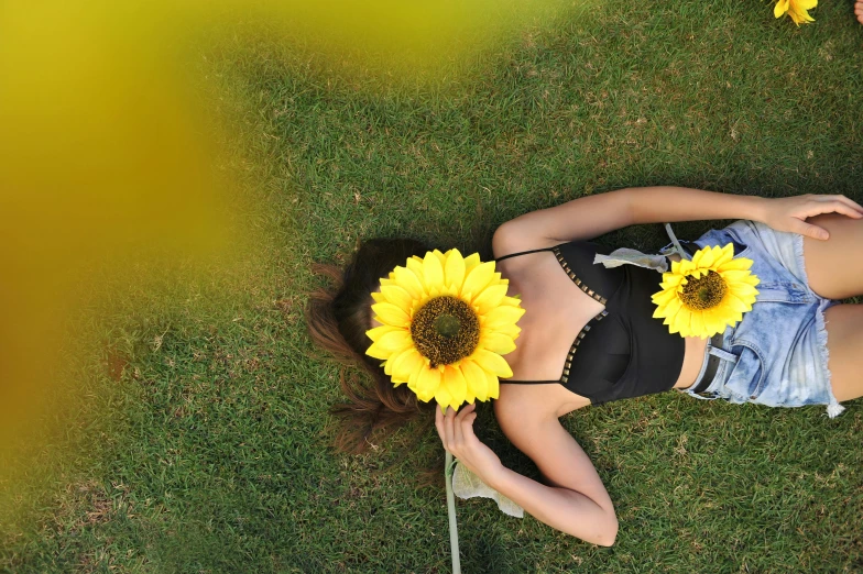 a woman laying in the grass with sunflowers on her head, inspired by Ren Hang, pexels contest winner, gardening, black, top-down shot, panoramic view of girl
