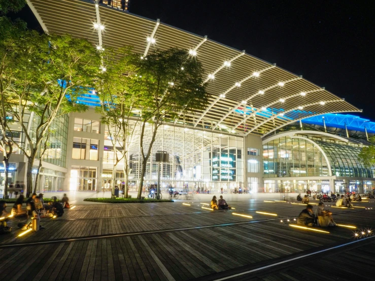 a group of people sitting on benches in front of a building, malls, it is night time, at night, pavilion