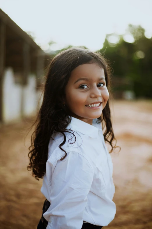 a little girl that is standing in the dirt, wearing a white button up shirt, arab ameera al-taweel, with textured hair and skin, medium close up shot