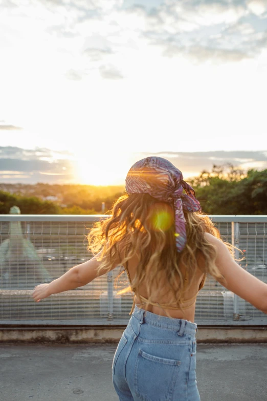 a woman riding a skateboard across a bridge, by Niko Henrichon, trending on pexels, happening, sunset halo behind her head, rooftop party, wearing a head scarf, flowing long hair