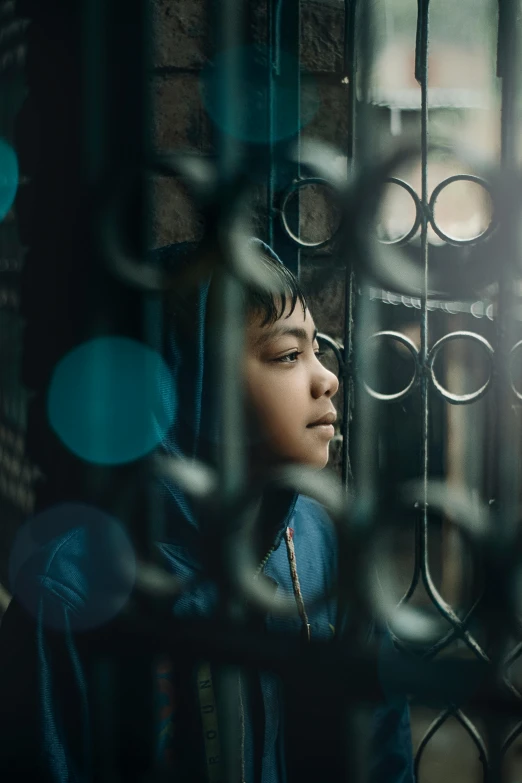 a young boy standing in front of a gate, inspired by Steve McCurry, unsplash contest winner, window ( city ), depressed girl portrait, bokeh”, jakarta