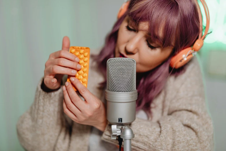 a woman holding a pill in front of a microphone, by Adam Marczyński, trending on pexels, realism, honeycomb, foam, rectangle, studio orange