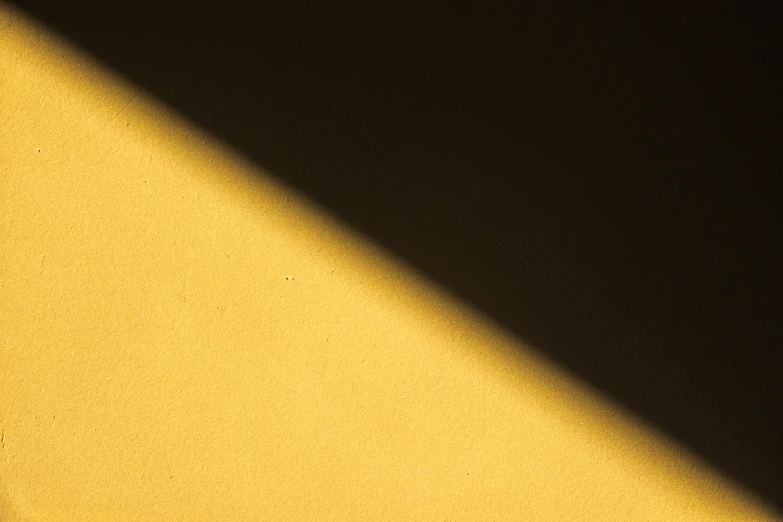 a clock sitting on top of a table next to a wall, unsplash, light and space, yellow awning, shadow play, (abstract), light - brown wall