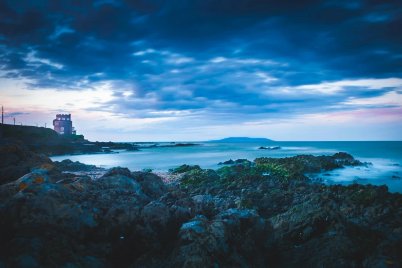 a lighthouse sitting on top of a rocky beach, dark castle setting, landscape photograph, conor walton, blue