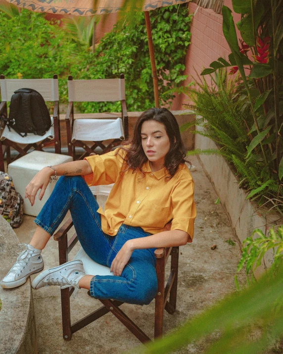 a woman sitting in a chair in a garden, an album cover, pexels contest winner, happening, wearing a modern yellow tshirt, isabela moner, at the terrace, nivanh chanthara