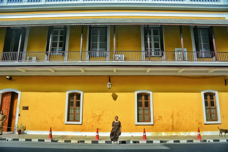 a woman standing in front of a yellow building, colonial exploration, jakarta, exterior photo, square