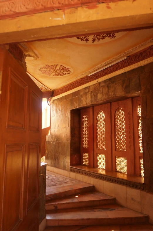 a wooden door and some stairs in a building, inspired by Osman Hamdi Bey, looking at the ceiling, red and white marble panels, amber, carved in wood