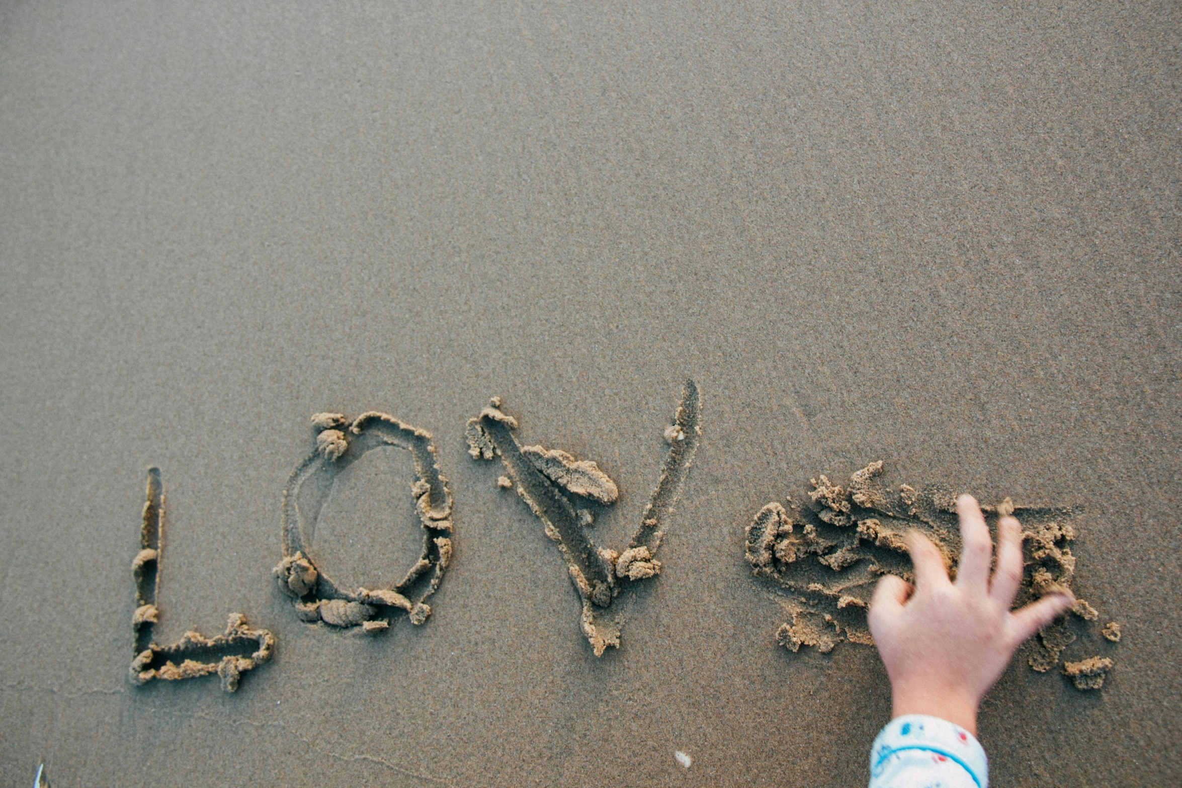 a person writing the word love in the sand, by Arabella Rankin, unsplash, land art, fan favorite, happy kid, thumbnail, shot on sony a 7