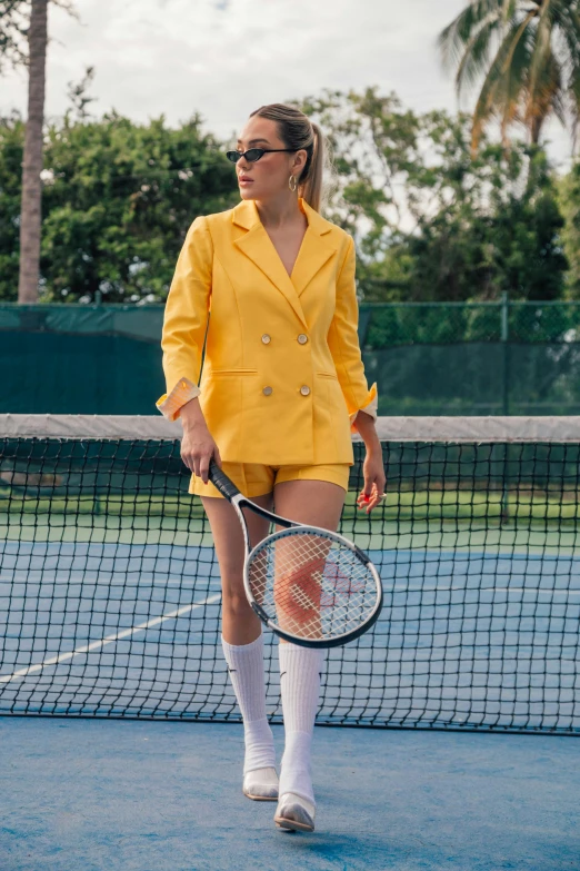 a woman standing on top of a tennis court holding a racquet, by Julia Pishtar, fine art, yellow carrera glasses, suit, in shorts, in the style wes anderson