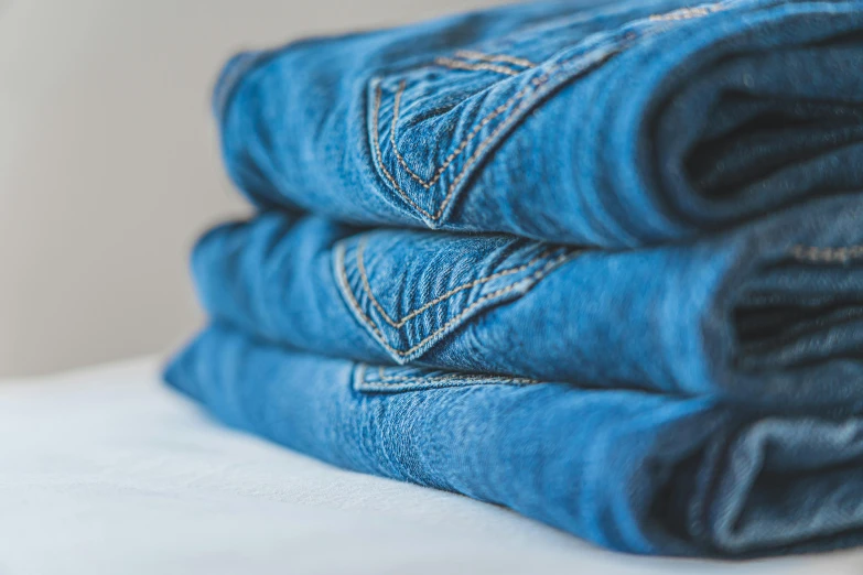 a stack of blue jeans sitting on top of a bed, by Sylvia Wishart, trending on unsplash, intricate detailing, carefully crafted, three views, folded