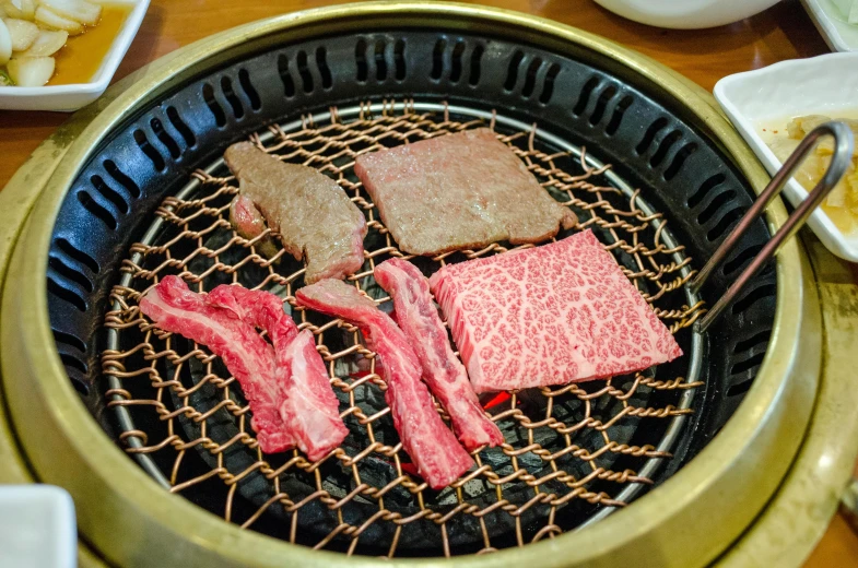 a close up of food on a grill on a table, mingei, 3 - piece, round, carnivore, gold