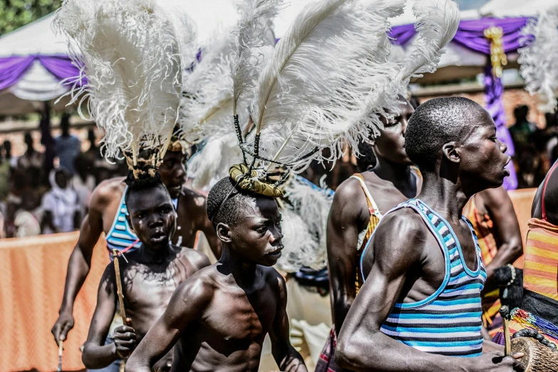 a group of people that are standing in the dirt, by Ingrida Kadaka, pexels contest winner, afrofuturism, covered in feathers, parade, cute boys, adut akech