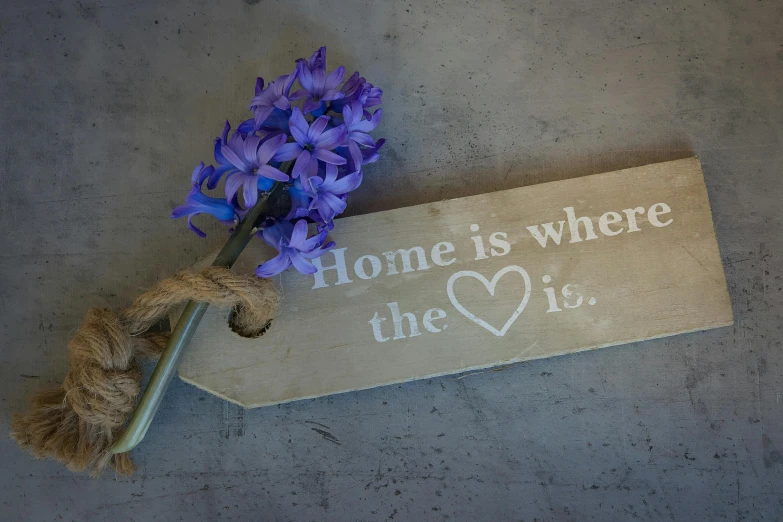 a wooden sign that says home is where the heart is, inspired by Tracey Emin, grape hyacinth, engraved blade, tag, carrying flowers