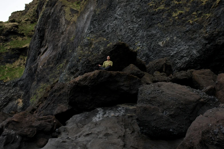 a man that is standing on some rocks, by Hallsteinn Sigurðsson, pexels contest winner, naturalism, sitting on the ground, cave entrance, sittin, slightly minimal