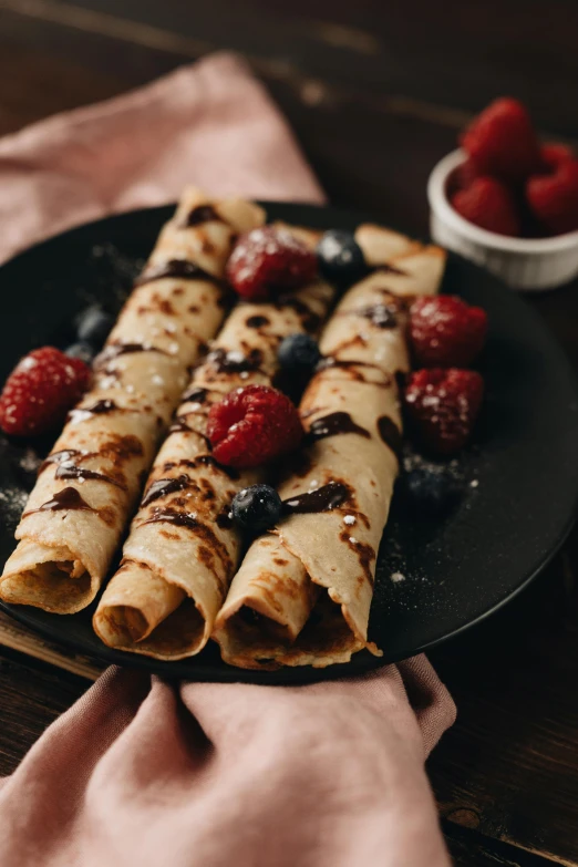 a black plate topped with crepes and raspberries, unsplash, sleek hands, 15081959 21121991 01012000 4k, cinnamon, rustic