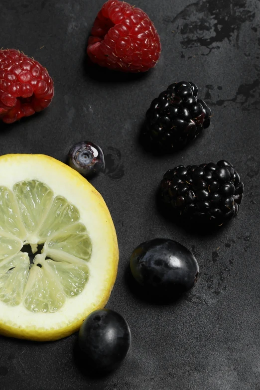 a lemon, raspberries, and blackberries on a table, zoomed in shots, on a gray background, on black paper, promo image