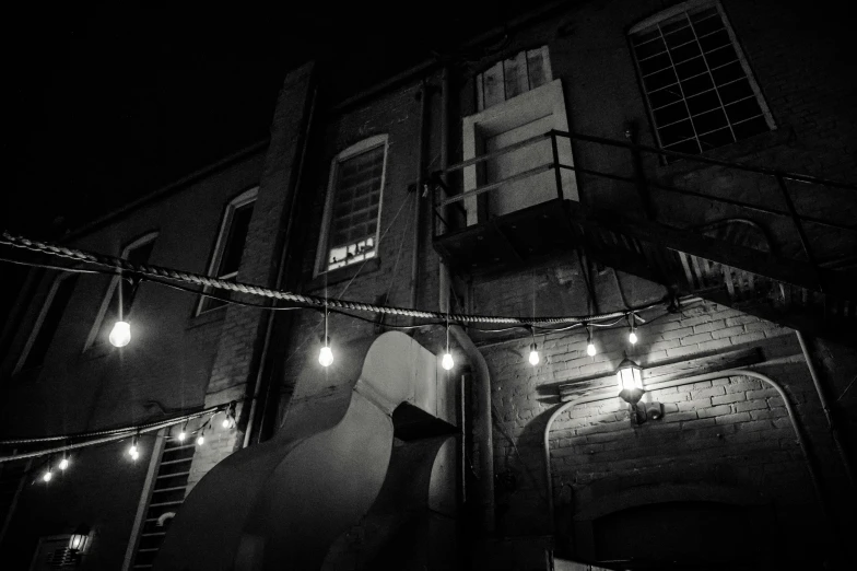 a black and white photo of a ghost in front of a building, by Dennis Flanders, unsplash, string lights, back alley, piano in the background, very low angle photograph