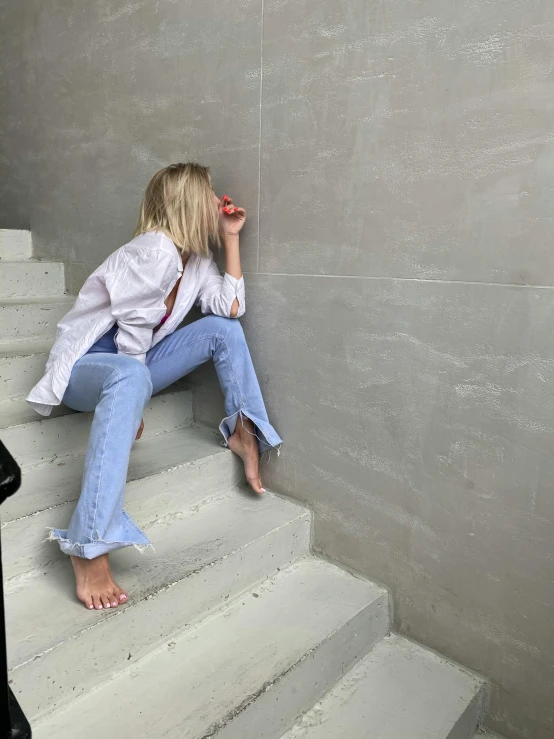 a woman sitting on a set of stairs talking on a cell phone, by Nina Hamnett, trending on unsplash, happening, pale blue outfit, jeans pants, cropped wide sleeve, white wrinkled shirt