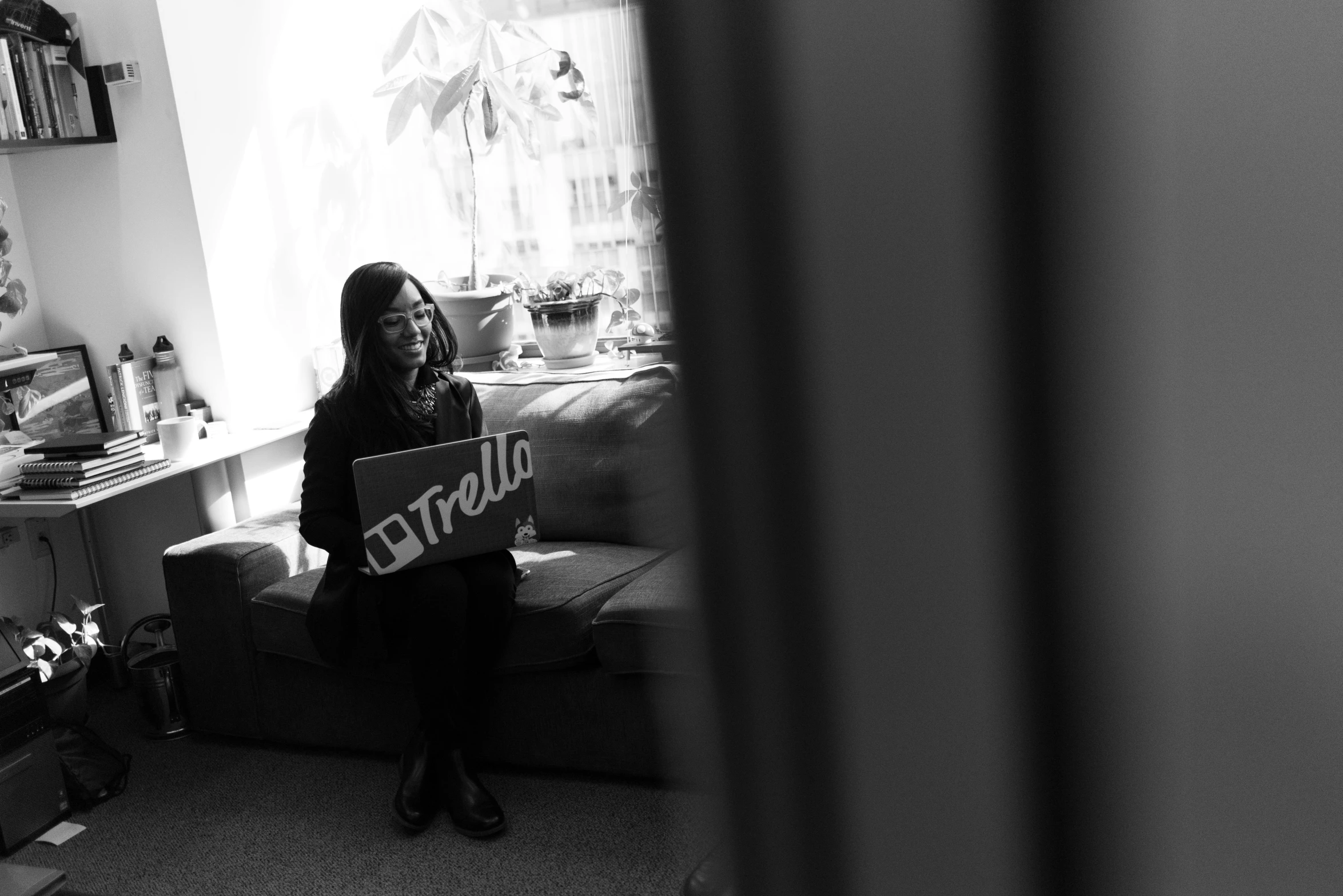 a woman sitting on a couch holding a sign, a black and white photo, by Mathias Kollros, unsplash, sitting at a computer, hello, gemma chen, near the window