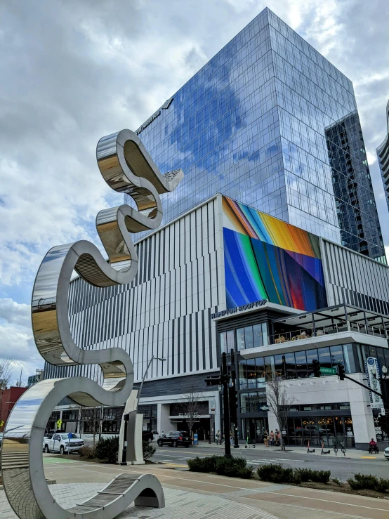 a large metal sculpture in front of a building, by Jeff Koons, pexels contest winner, rainbow tubing, highrise business district, southdale center, sephora