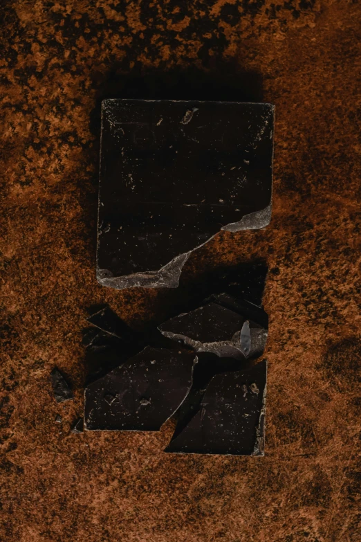 a piece of chocolate sitting on top of a table, inspired by Alberto Burri, unsplash, renaissance, panel of black, shattered earth, detailed product image, charred
