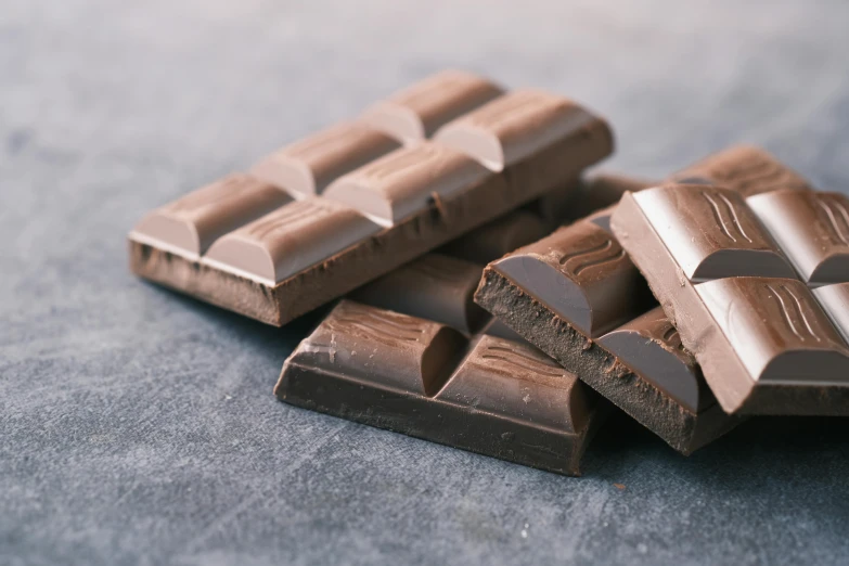 three pieces of chocolate sitting on top of a table, by Helen Stevenson, trending on pexels, hurufiyya, asset on grey background, dark brown, rectangular, chewing