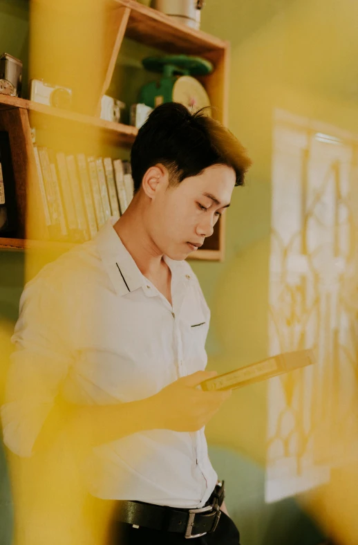 a man in a white shirt and black pants, a picture, inspired by jeonseok lee, pexels contest winner, using a magical tablet, yellow hue, headshot profile picture, dusty library