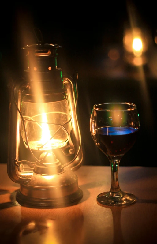 a candle and a glass of wine on a table, pexels, carbide lamp, warm lantern lighting, with blue light inside, promo image