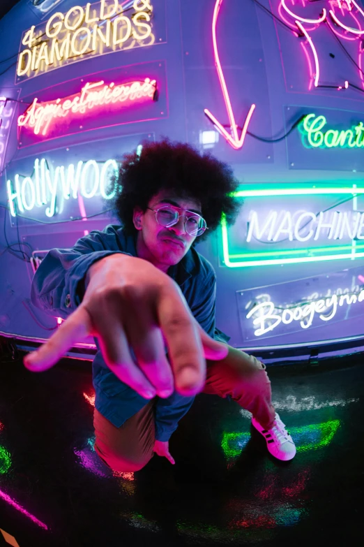 a man sitting on top of a car in front of neon signs, inspired by David LaChapelle, trending on pexels, curly afro, pointing at the camera, zayn malik, holy machine