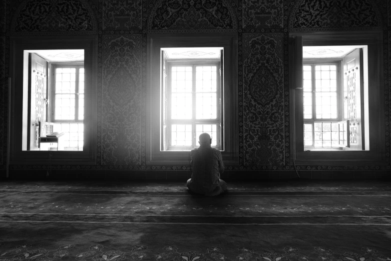 a person sitting on the floor in front of two windows, a black and white photo, by Niyazi Selimoglu, pexels contest winner, islamic art, sunrise coloring the room, sultan, godly