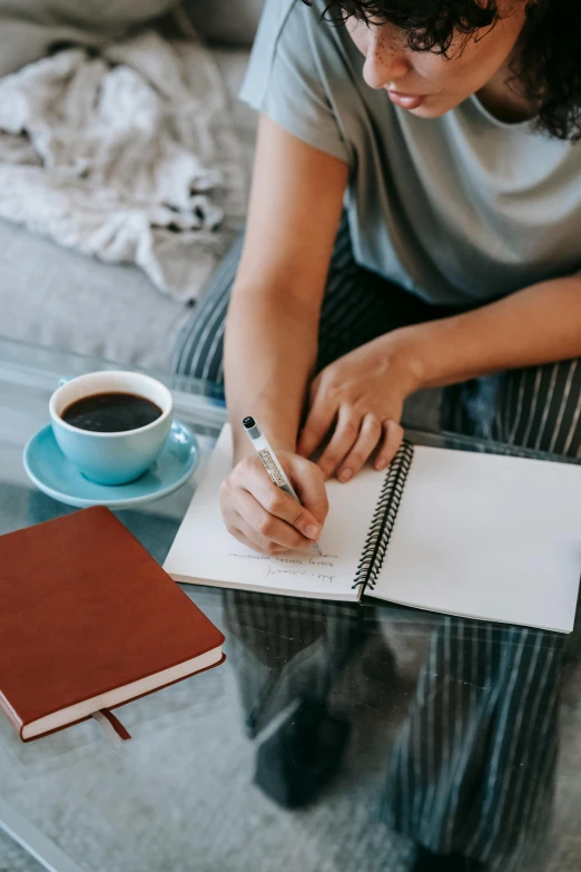 a woman sitting on a couch writing in a notebook, by Nicolette Macnamara, cup of coffee, thumbnail, high quality paper, sydney hanson