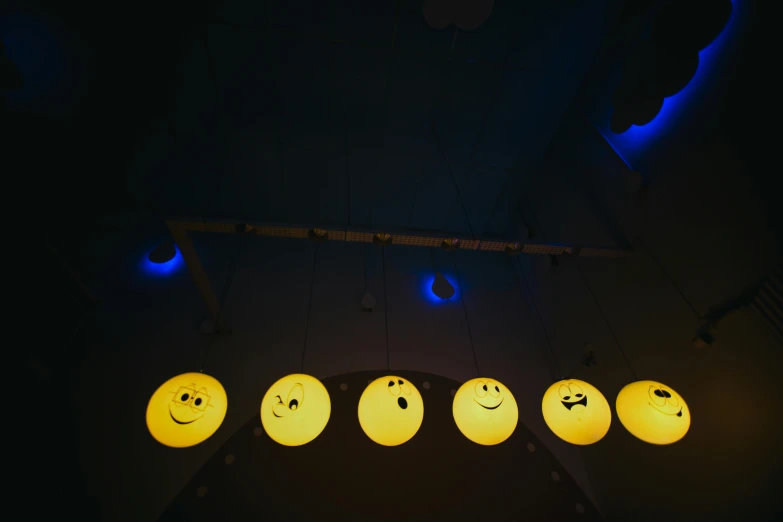 a bunch of smiley faces hanging from a ceiling, by Attila Meszlenyi, trending on pexels, light and space, night light, yellow and blue, lunar cycles, front lit