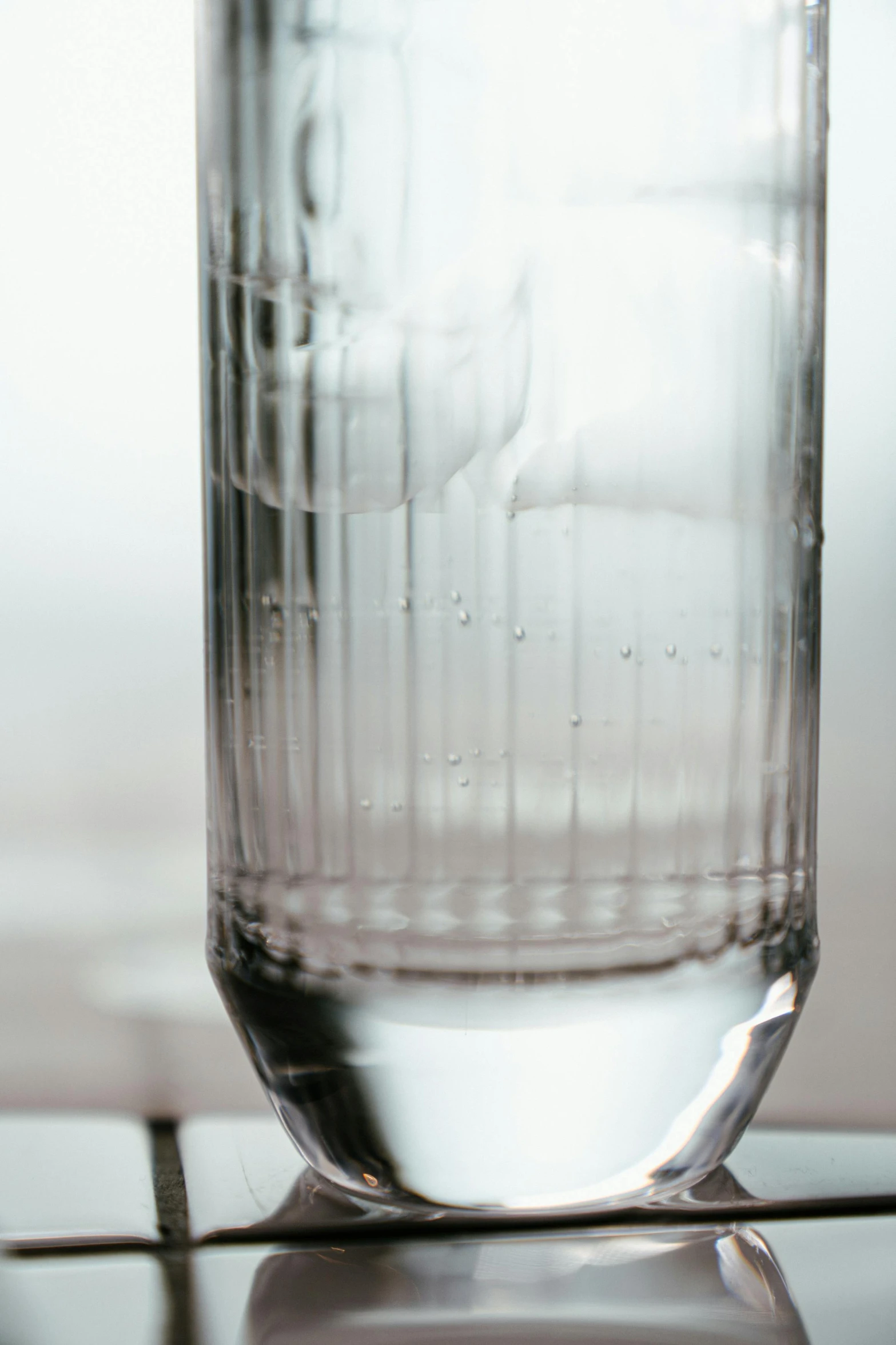 a glass of water sitting on top of a table, an etching, unsplash, photorealism, high detailed close up of, straight smooth vertical, transparent corrugated glass, bubbly